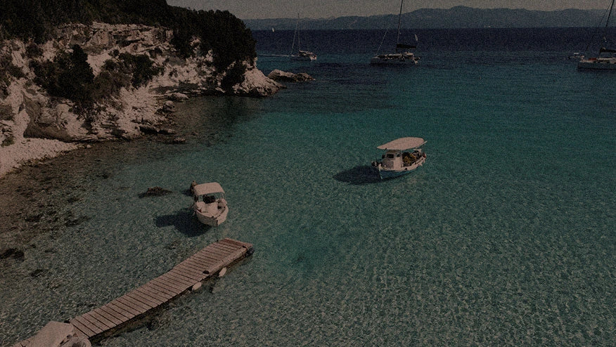 Vista de enseada no verão europeu com mar cristalino, barcos ancorados e píer de madeira em cenário de viagem entre destinos