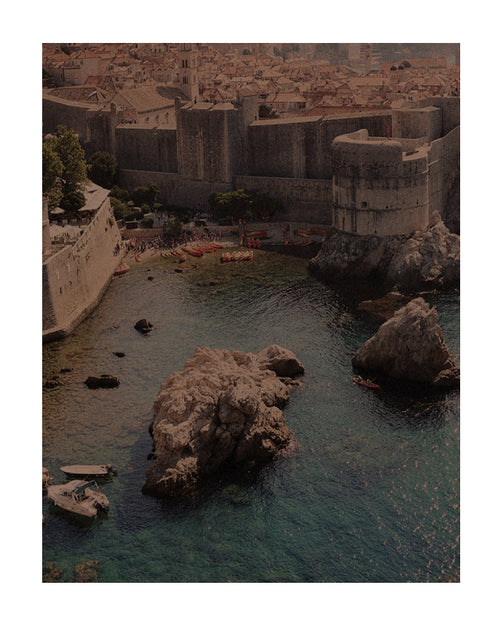 Vista costeira no verão europeu com muralhas de cidade histórica, mar cristalino, barcos e rochedos à beira da água