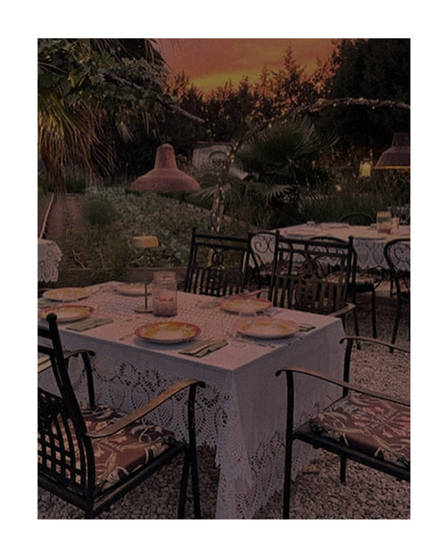 Jantar ao ar livre no verão europeu, com mesa posta em jardim, cadeiras de ferro e atmosfera aconchegante ao entardecer