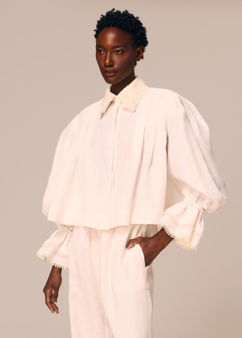 Detalhe da camisa feminina off White Essência La Gea com pregas frontais, duplo babado nos punhos e renda guipir no colarinho