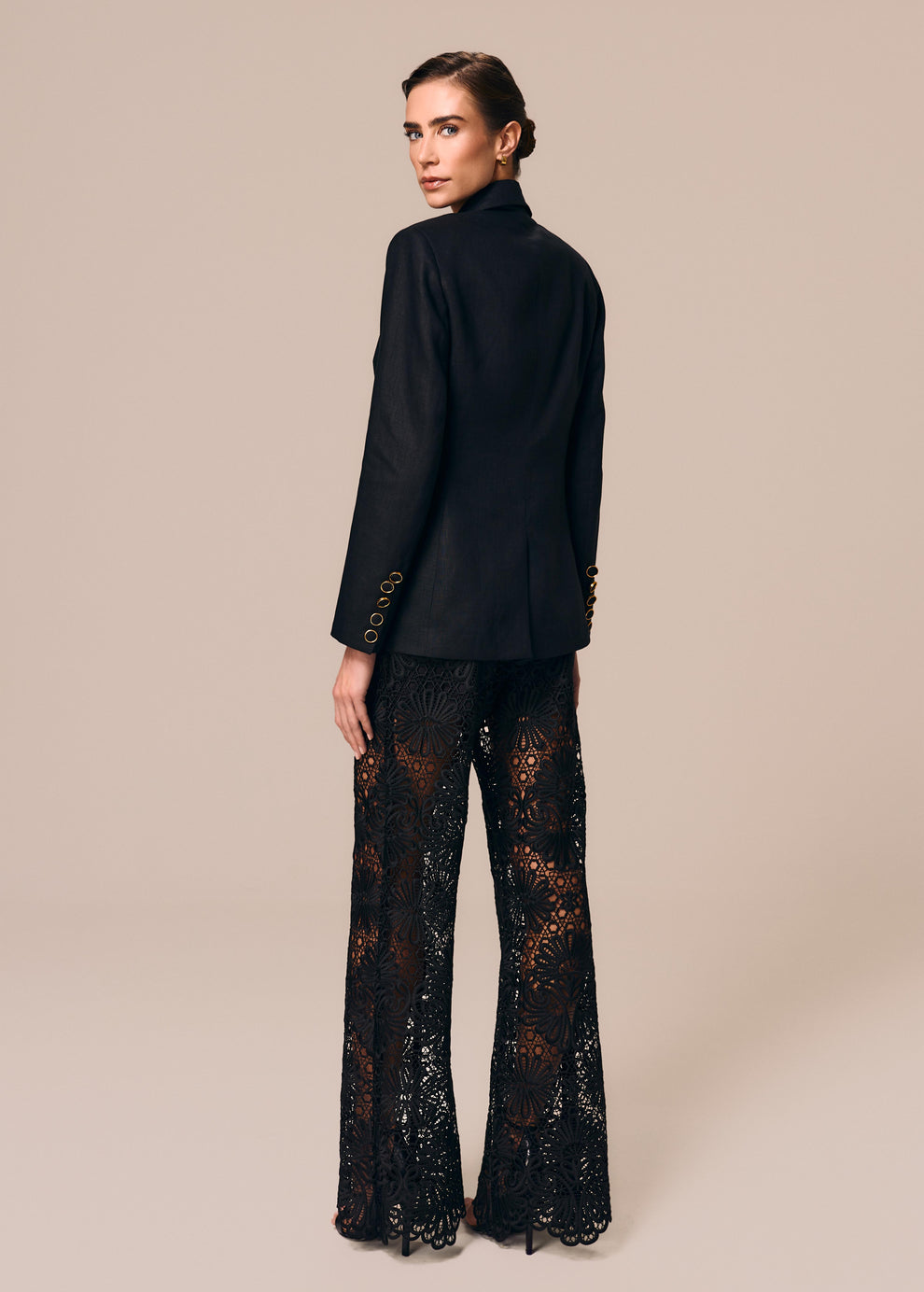Modelo de costas veste blazer alfaiataria preto Essência com calça flare em renda preta Cerâmica La Gea