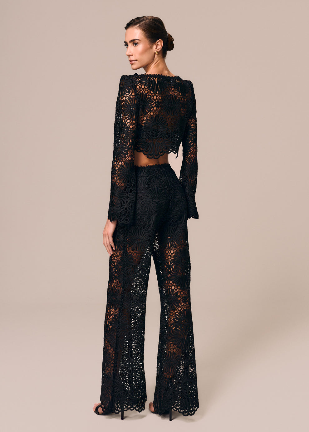 Modelo de costas combina calça flare em renda preta com top cropped manga longa Cerâmica La Gea