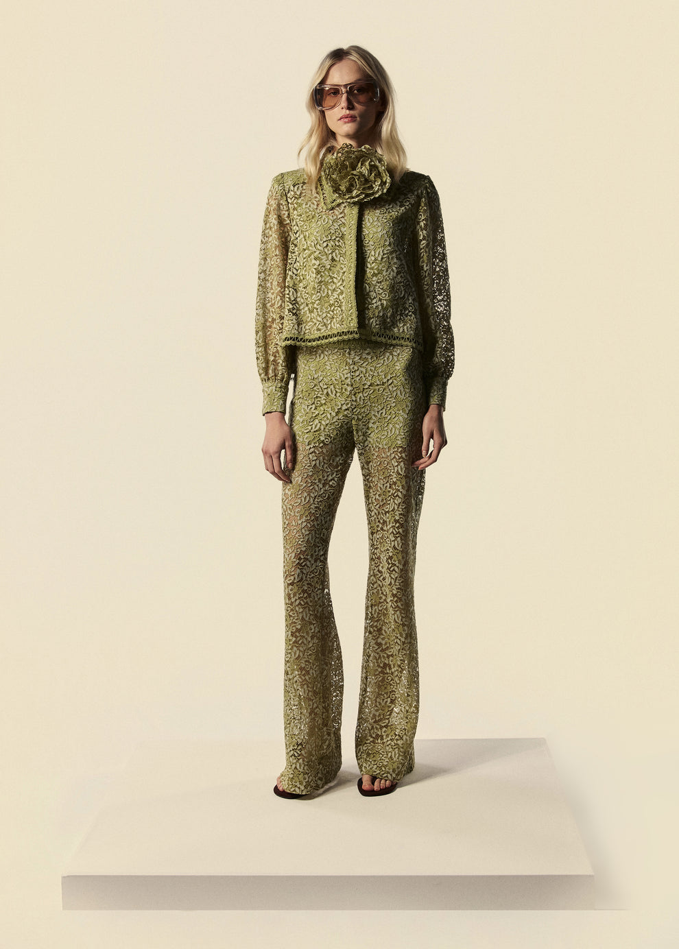Modelo combina calça flare de renda com camisa feminina e cinto utilizado como colar de flores. Peças da família Bosque da La Gea.
