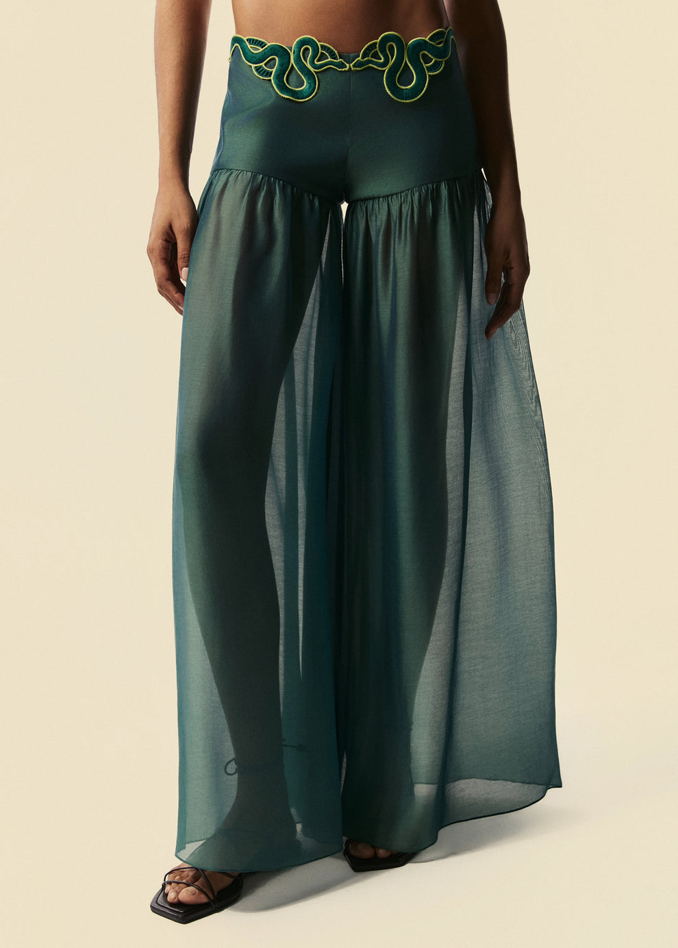 A calça pantalona verde Destino possui comprimento das pernas em tecido fluido e aplicação de guipir de serpentes no cós.