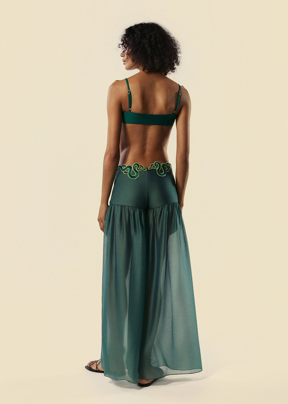 Modelo de costas com a calça pantalona verde Destino com o top de biquíni triângulo da família Trincas do lançamento da La Gea.