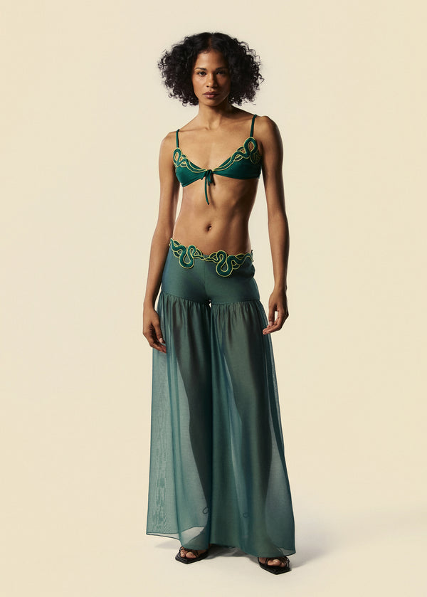 Modelo combina a calça pantalona verde Destino e o top de biquíni Trincas do verão 27 da La Gea com rasteirinha preta de tiras.
