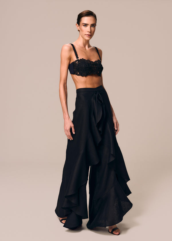 Modelo veste calça pareô preto com babados e amarração Essência La Gea e top de biquíni bandeau de renda Pedra