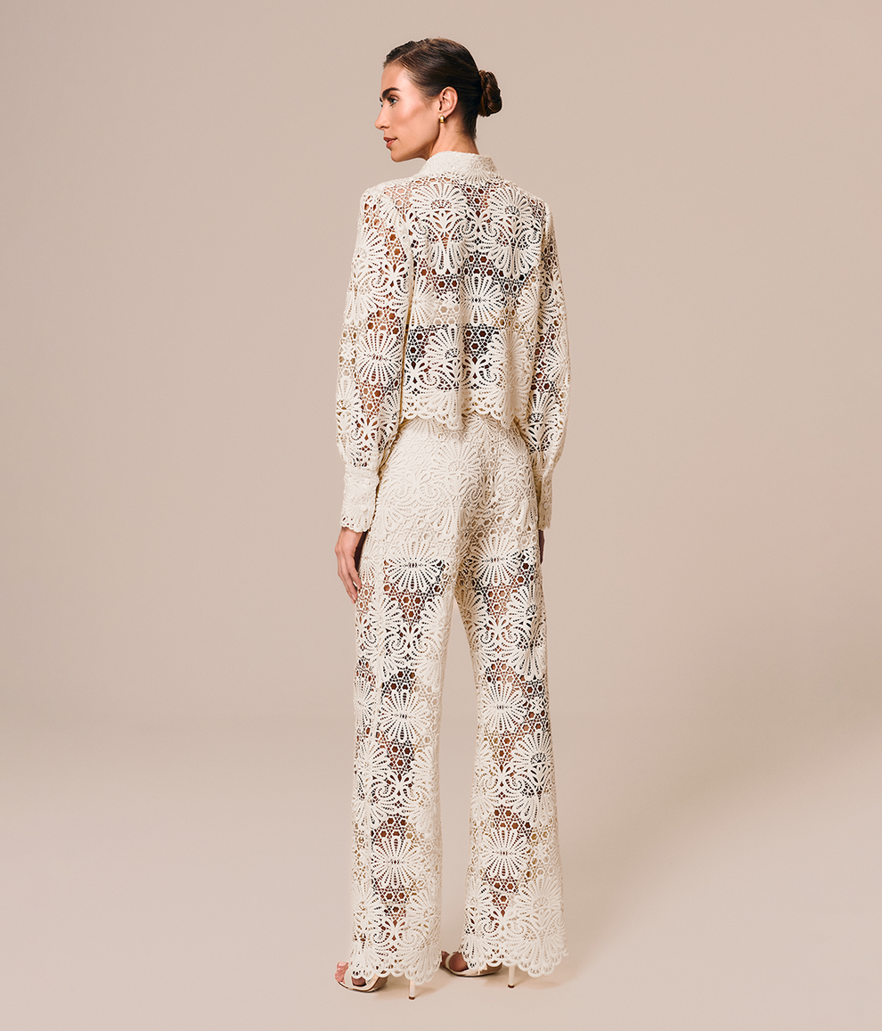 Modelo de costas veste look off white com camisa feminina e calça flare de renda Cerâmica La Gea