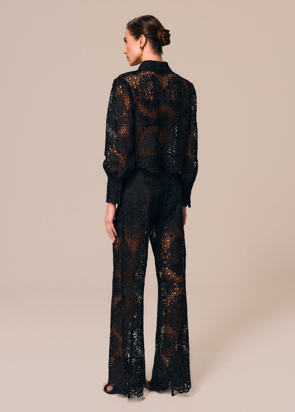 Modelo de costas veste look preto com camisa feminina e calça flare de renda Cerâmica La Gea