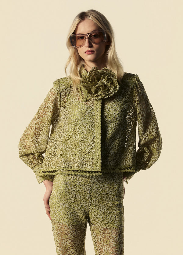 Modelo combina camisa feminina de renda com calça flare e adiciona broche de flor na gola. 