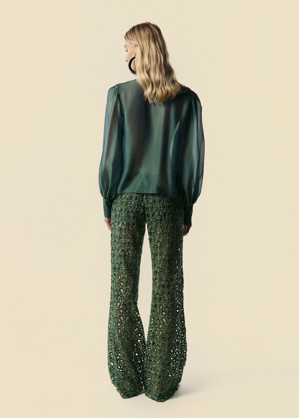 Modelo de costas combina camisa feminina verde Destino com transparência e calça flare de renda Trilhas do lançamento da La Gea.