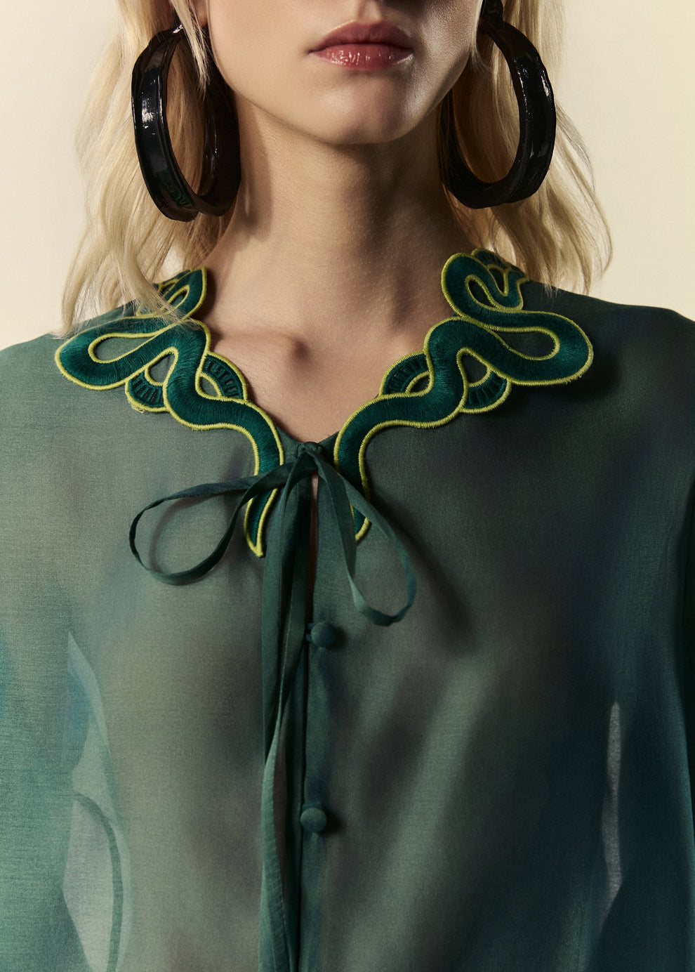 Detalhe da gola da camisa feminina verde com acabamento em renda de serpente e amarração.