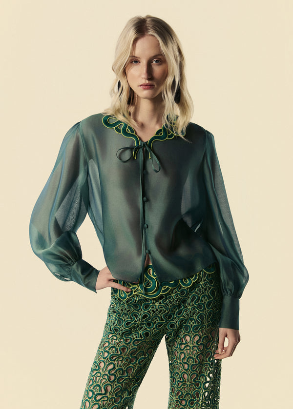 A camisa feminina verde Destino com transparência e detalhe de renda no colarinho com amarração.