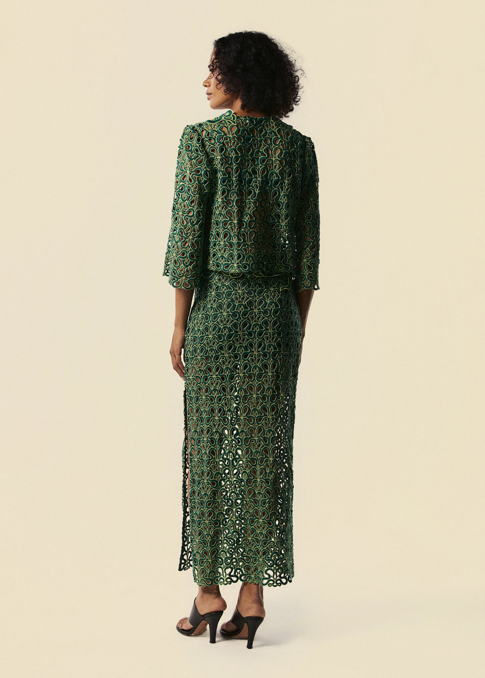 Modelo de costas com camisa feminina em renda verde com detalhe sem serpentes e saia longa do lançamento da La Gea.