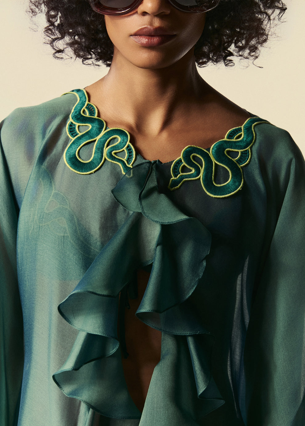 O kaftan curto verde Destino apresenta babados na parte frontal e aplicação de guipir de serpente no decote. 