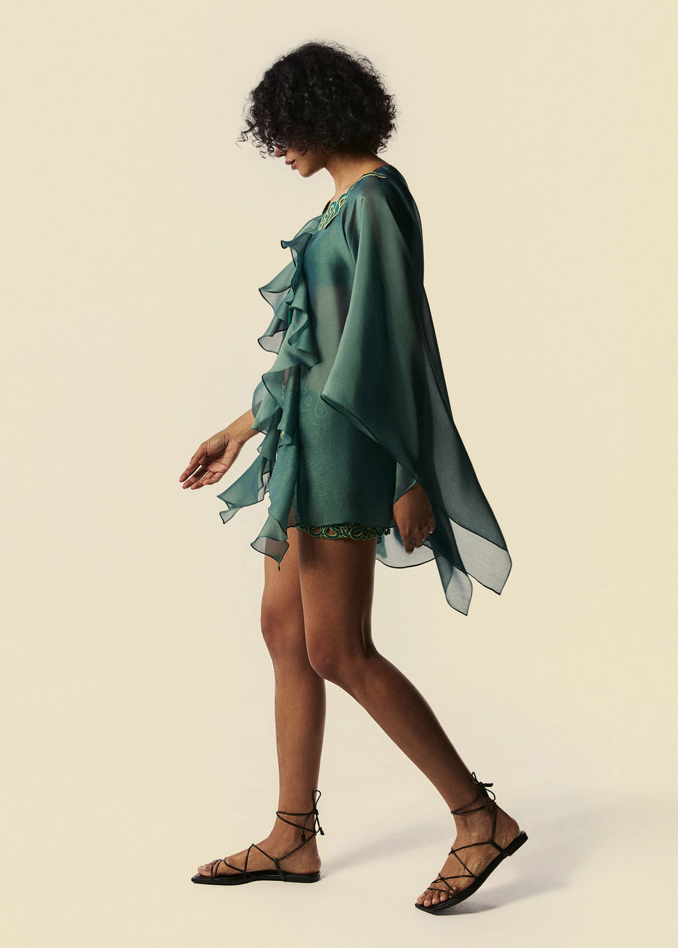 Modelo caminha com kaftan curto verde Destino e shorts curto Trilhas da La Gea com rasteirinha de tiras preta.