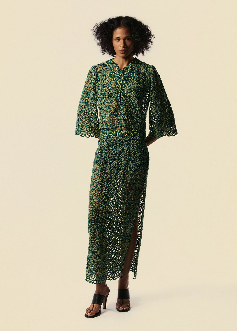 Modelo usa saia longa de renda verde com camisa de mangas 3/4. Combina com sandália de salto preto.