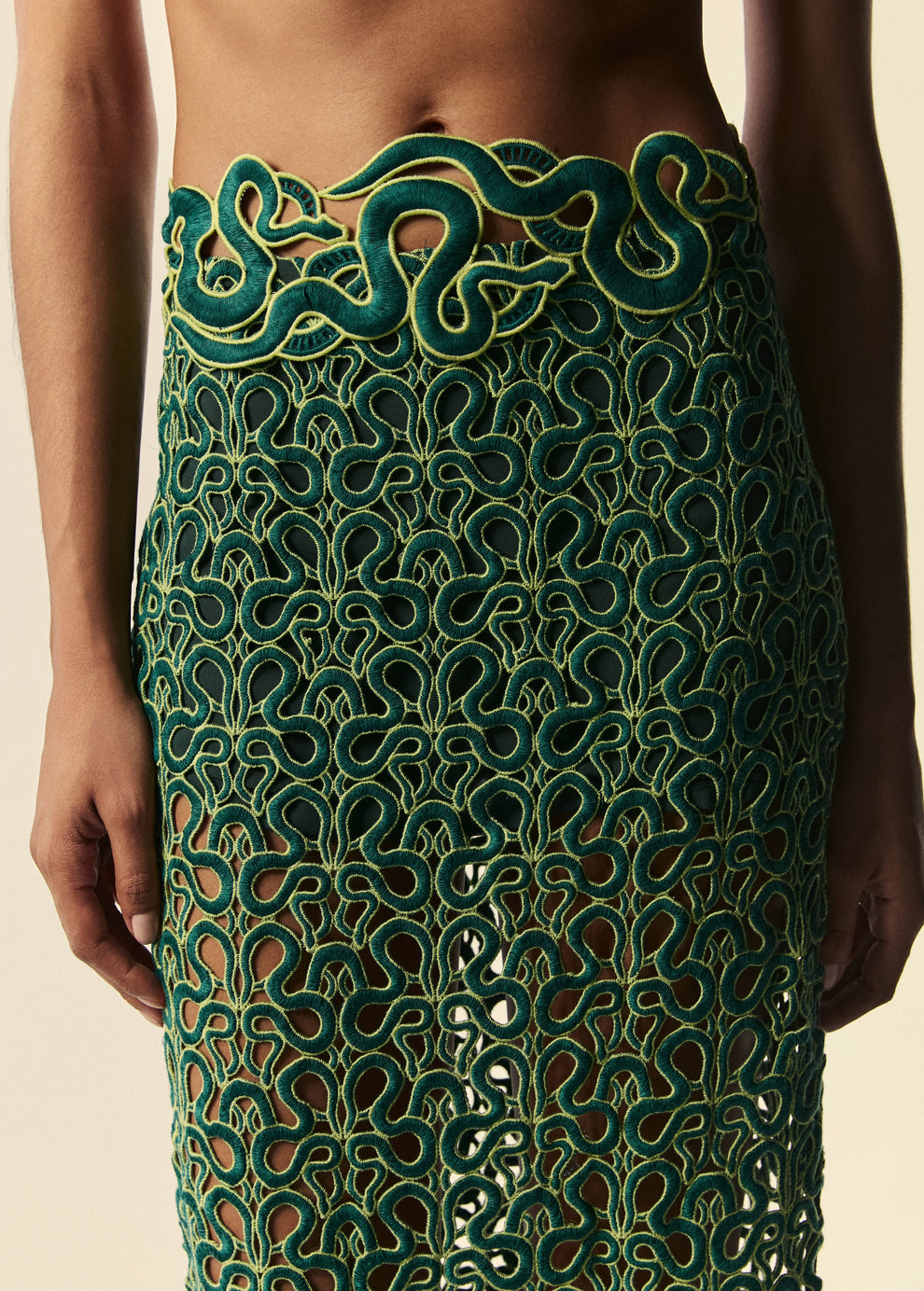 Detalhe da saia longa de renda verde com desenhos de serpentes.
