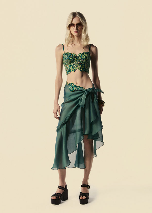 Modelo veste saia pareô longa verde Destino com corset Trilhas. Combina com óculos escuro e sandália de plataforma preta. 