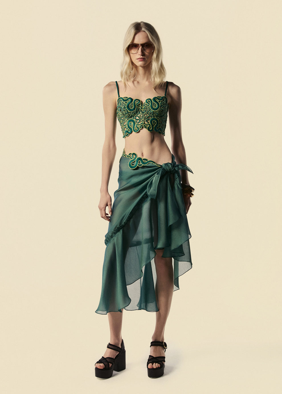 Modelo veste saia pareô longa verde Destino com corset Trilhas. Combina com óculos escuro e sandália de plataforma preta. 