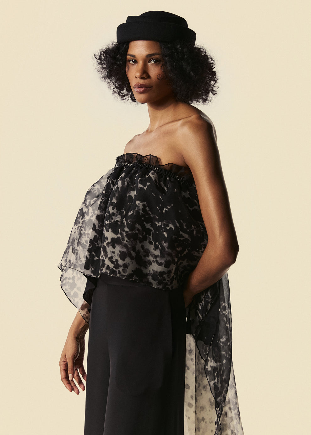 Modelo usa top tomara que caia em seda estampada com chapéu preto. Blusa com volume delicado e assimetria nas costas.