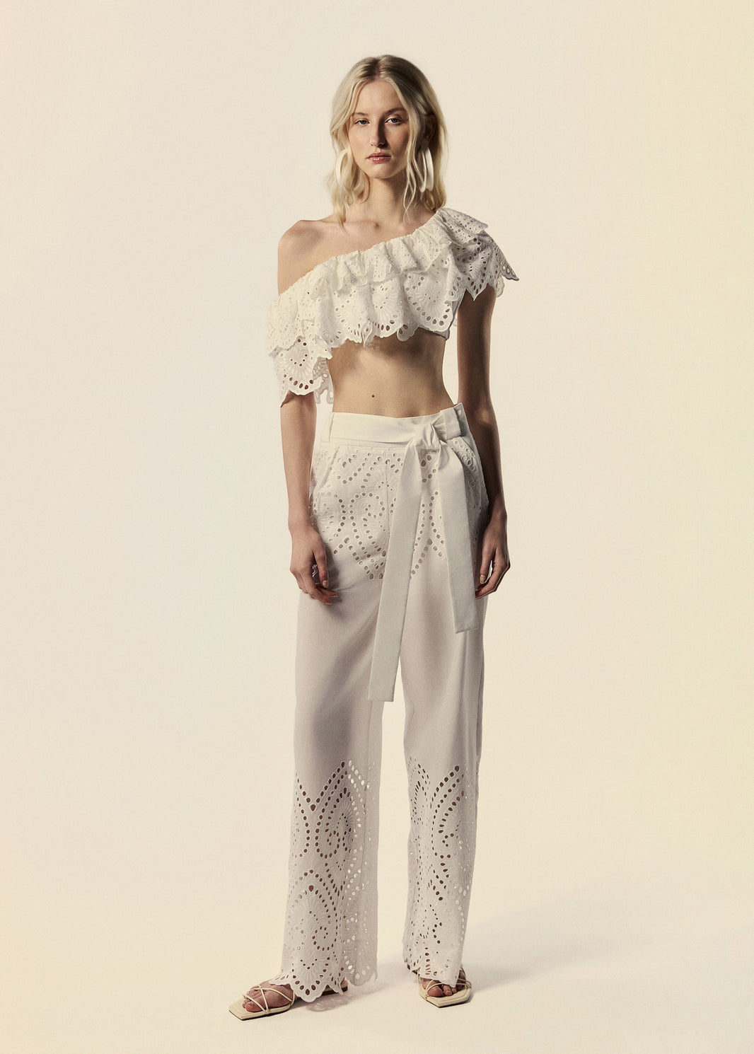 Modelo combina o top de um ombro só branco La Gea com calça pantalona em laise de algodão.