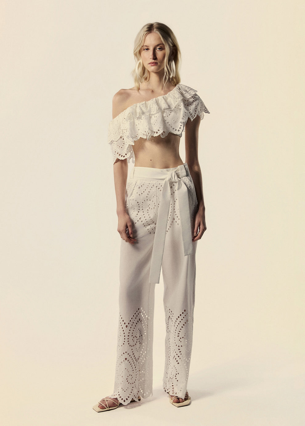 Modelo combina o top de um ombro só branco La Gea com calça pantalona em laise de algodão.