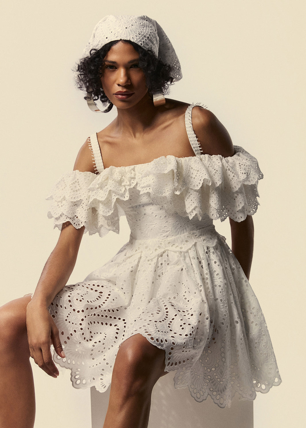 Pose da modelo sentada com o vestido curto ombro a ombro em laise branco da família Lumina da La Gea.