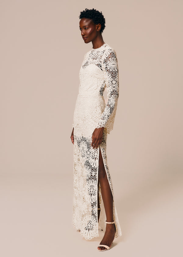 Modelo usa vestido longo com manga longa e fenda lateral em renda off White Cerâmica La Gea