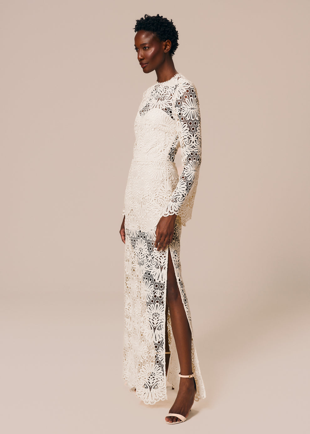 Modelo usa vestido longo com manga longa e fenda lateral em renda off White Cerâmica La Gea
