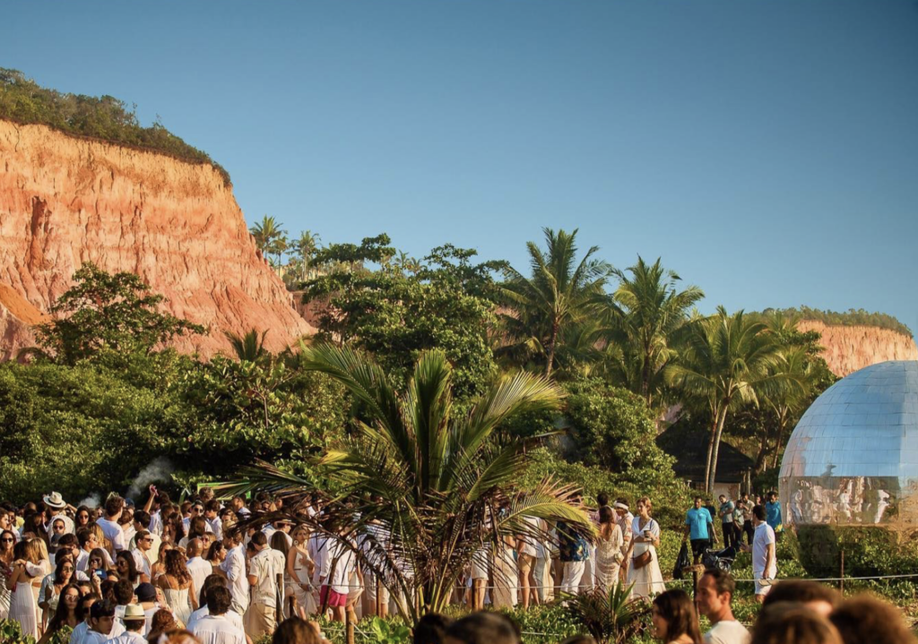 Imagem com várias  pessoas vestidas de branco em uma festa, tendo como fundo uma montanha e árvores]